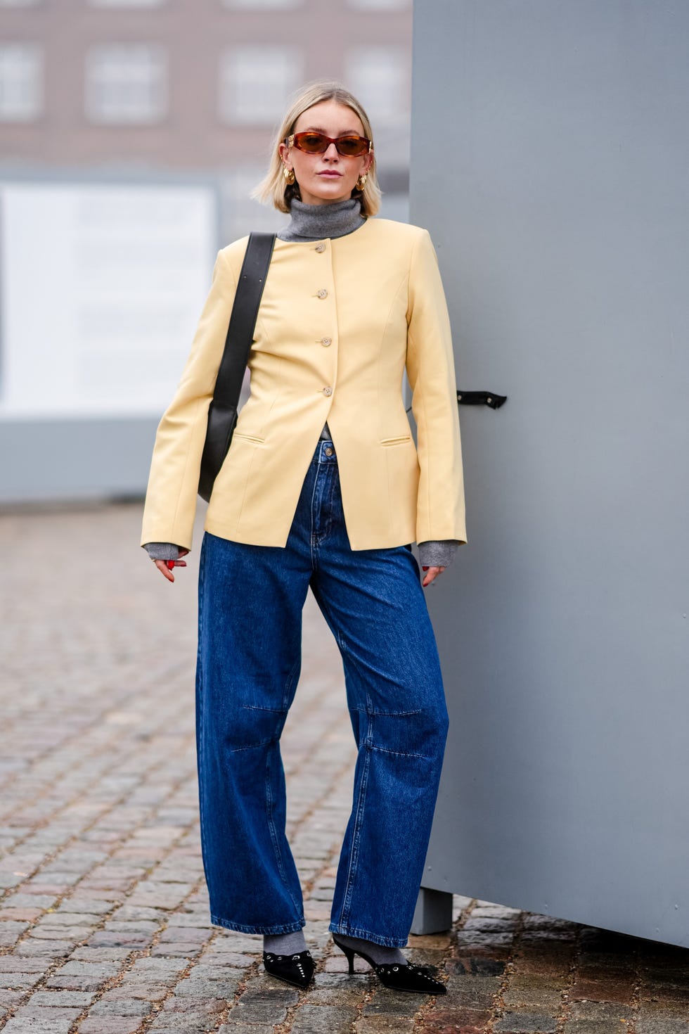 copenhagen, denmark january 30 a guest wears miu miu sunglasses, golden earrings, a pale pastel yellow jacket, a black leather bag, blue denim jeans pants , pointed shoes, outside rolf ekroth, during the copenhagen fashion week aw24 on january 30, 2024 in copenhagen, denmark photo by edward berthelotgetty images