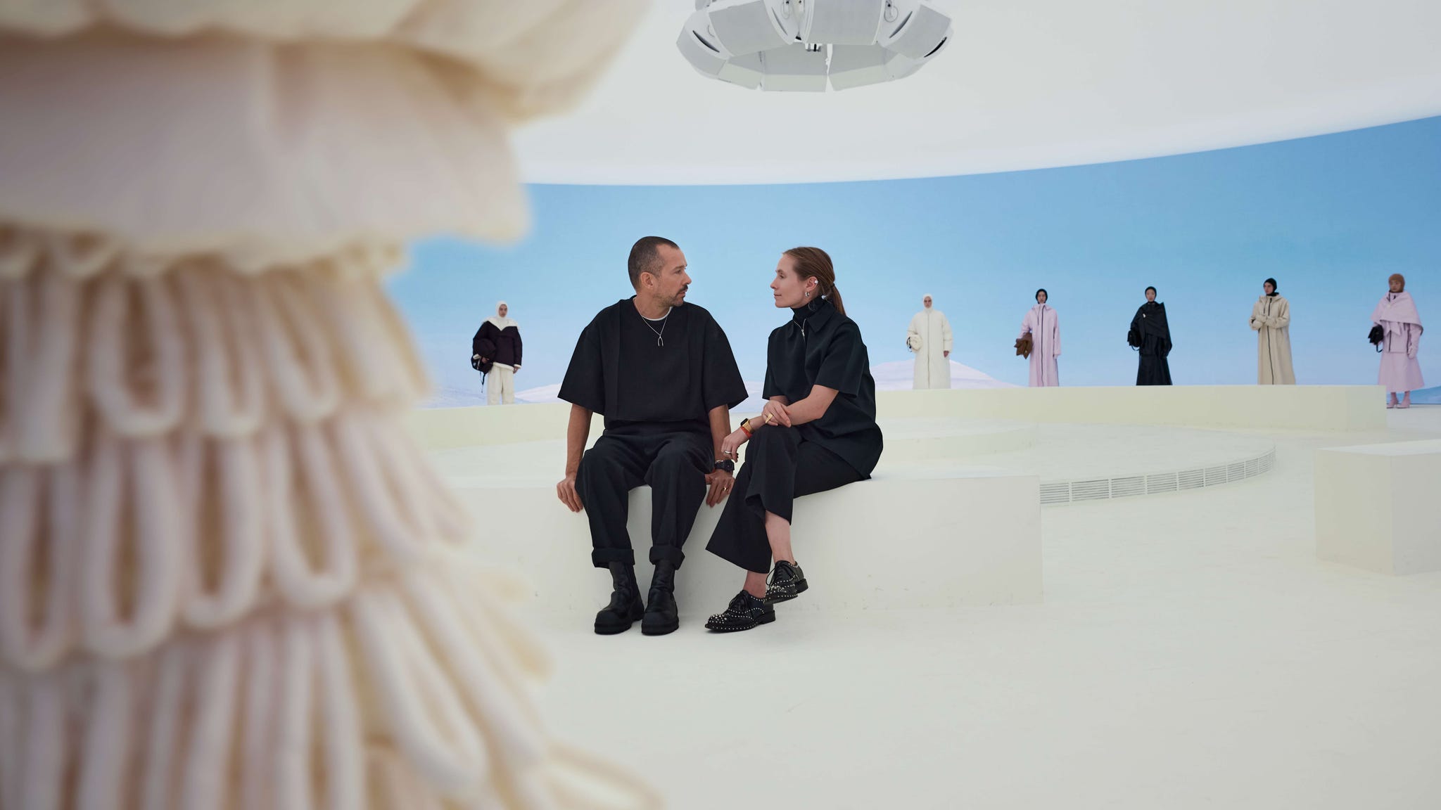 a man and woman sit together on a circular platform with a smooth white surface