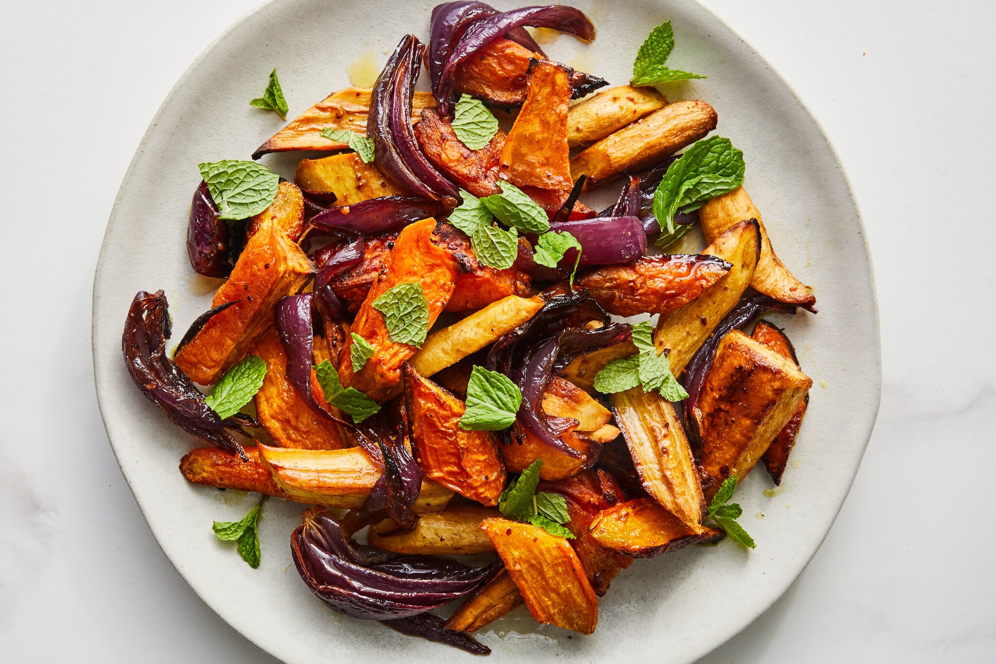 A white stone plate holds roasted carrots, squash and red onions.