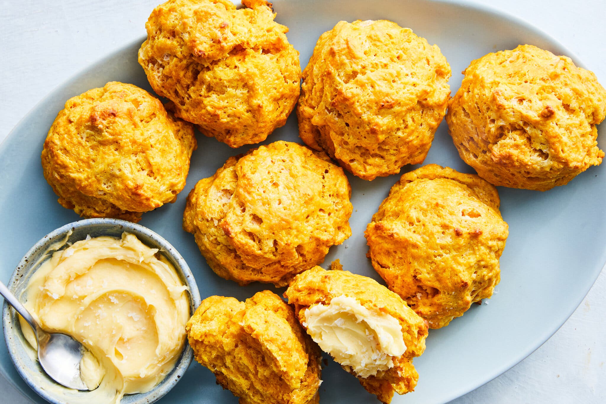 Big, round orange-colored biscuits are on a blue plate with butter.