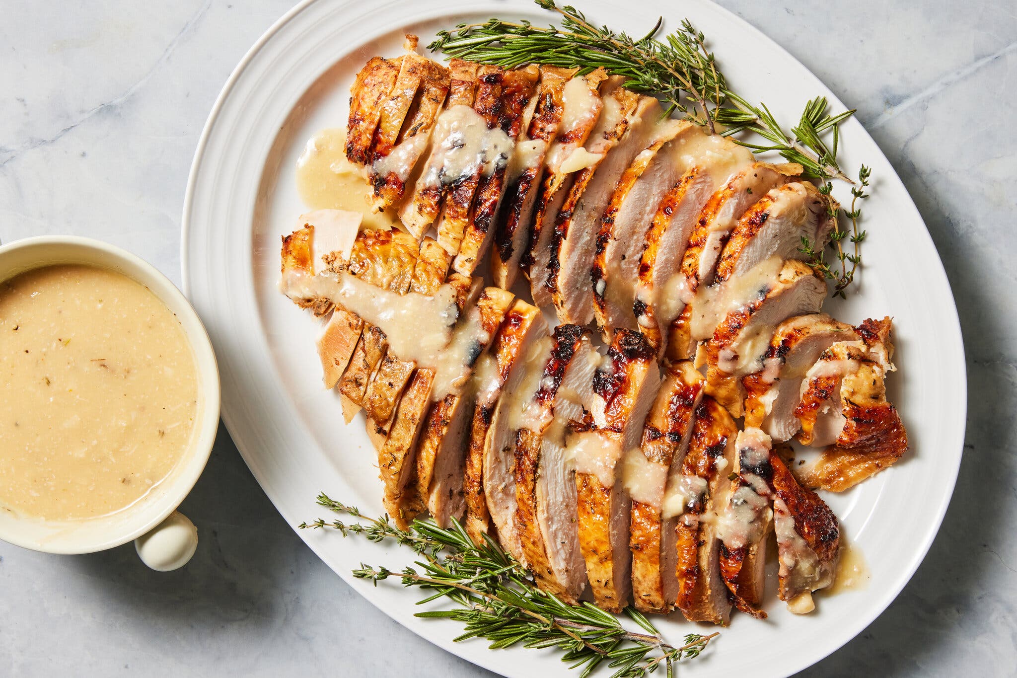 An oval white platter holds sliced turkey drizzled with gravy from the bowl next to it.