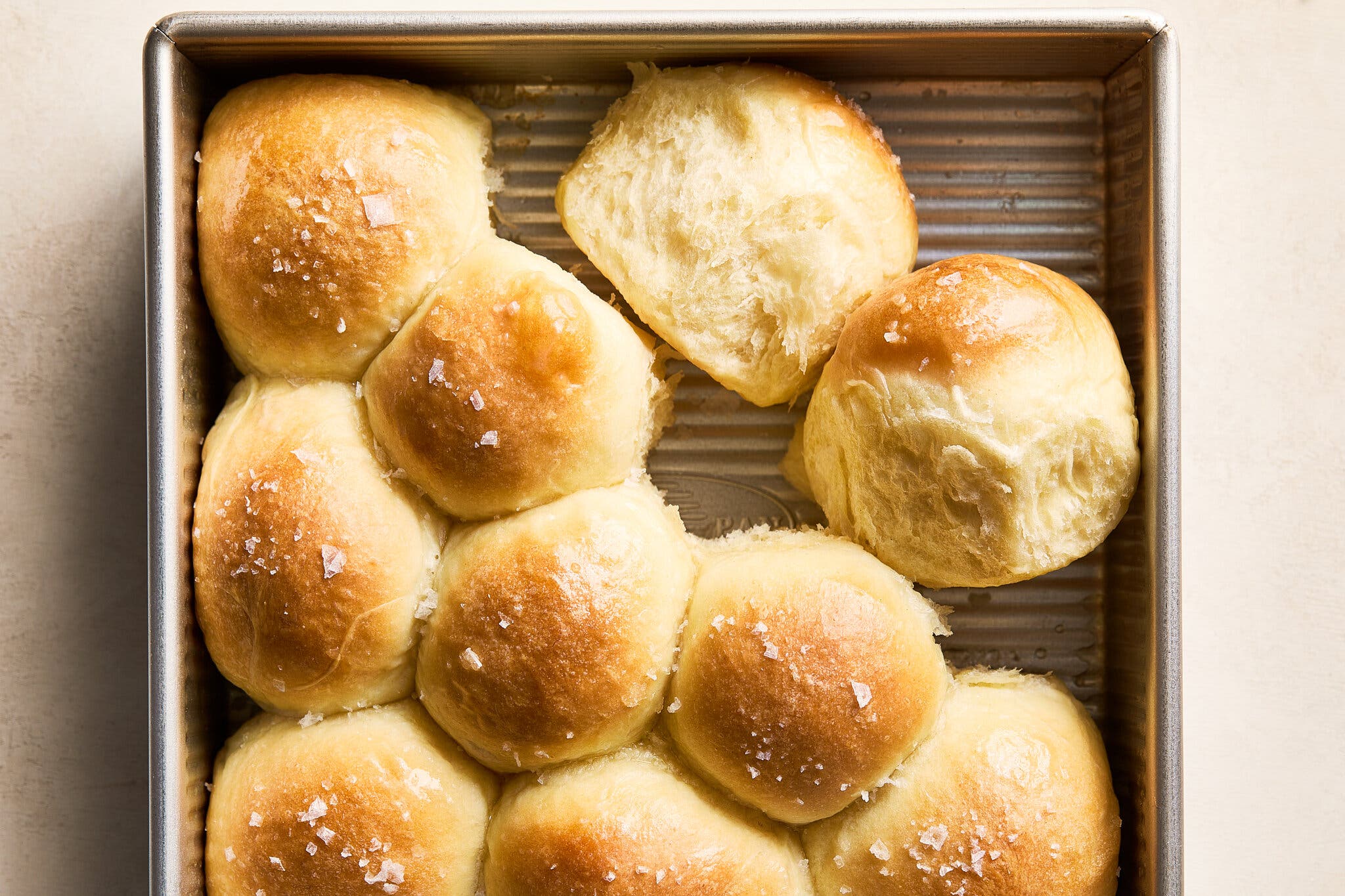 A baking pan is filled with round rolls with salt sprinkled on top.