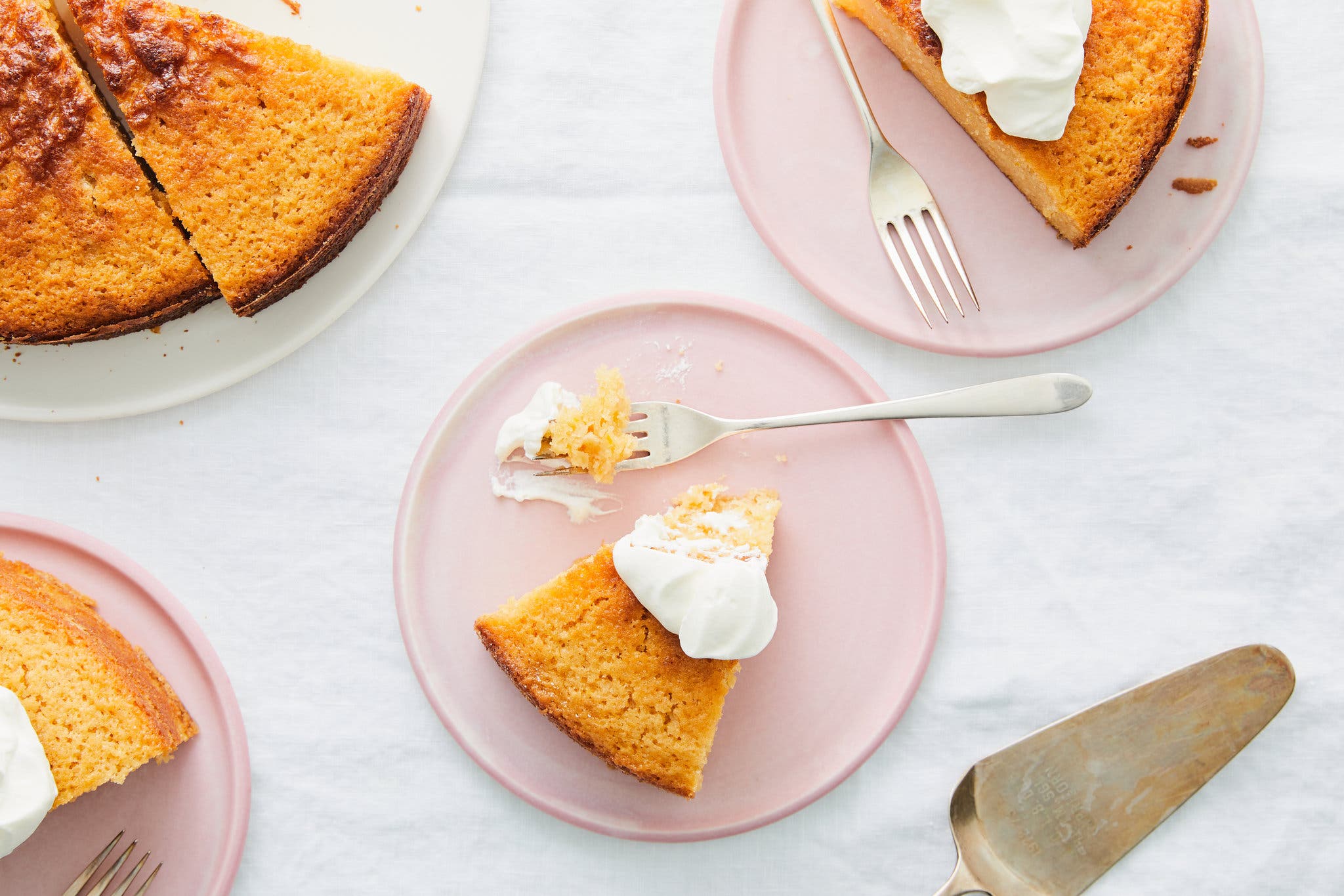 Three pink plates with a slice of cake topped with dollops of whipped cream.