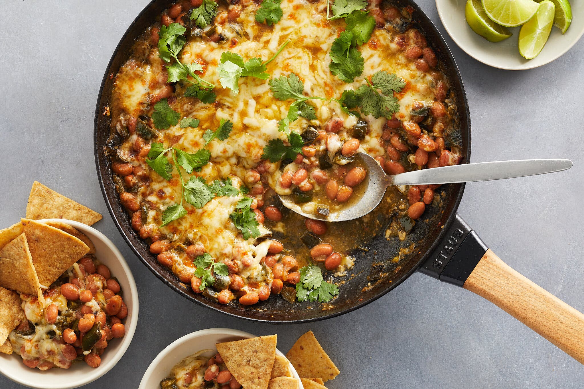 A cast-iron skillet is full of cheesy green chile bean bake with a scattering of cilantro and a spoon stuck in.