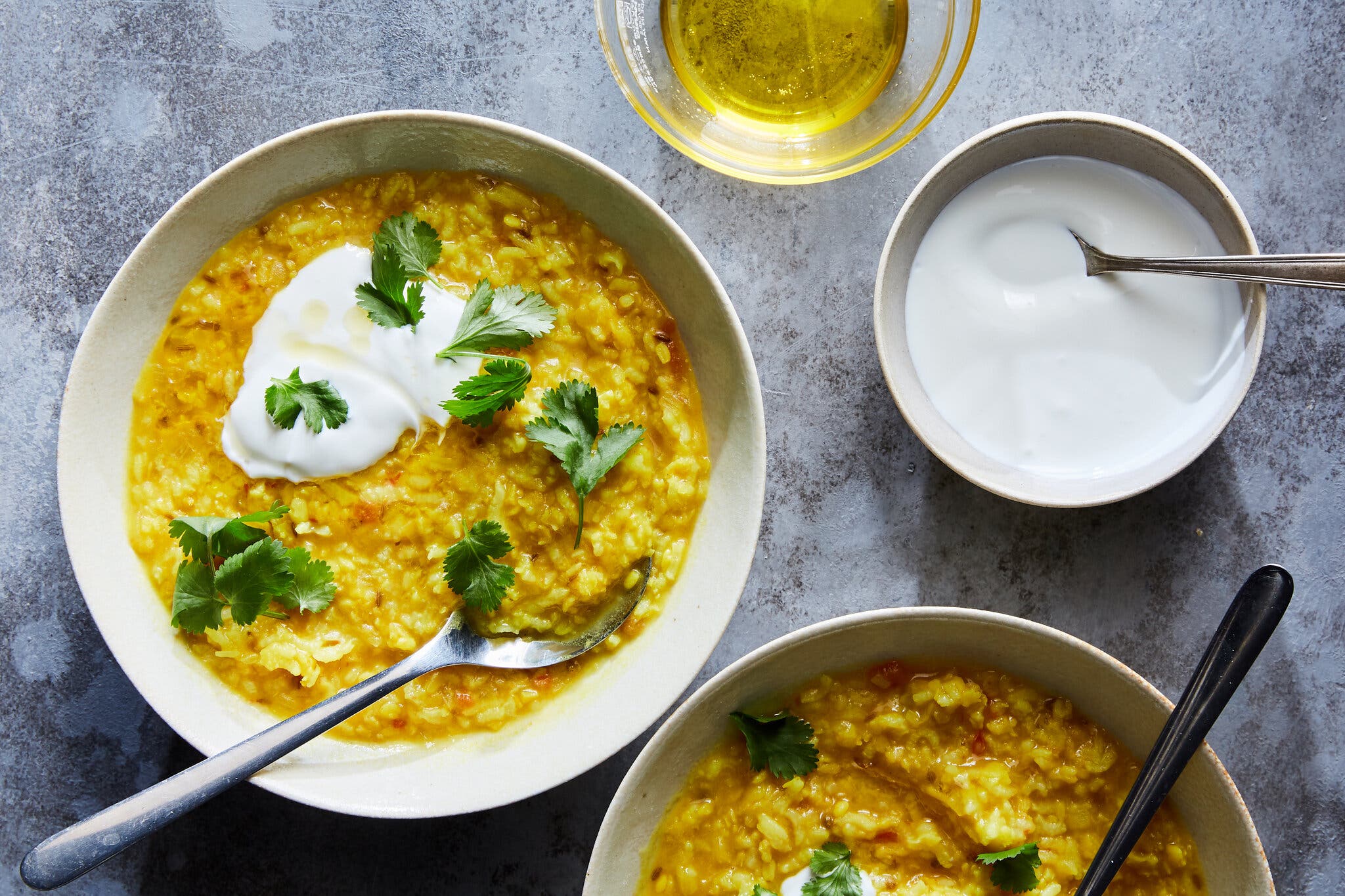 Two bowls of bright yellow khichdi are topped with yogurt and cilantro leaves.