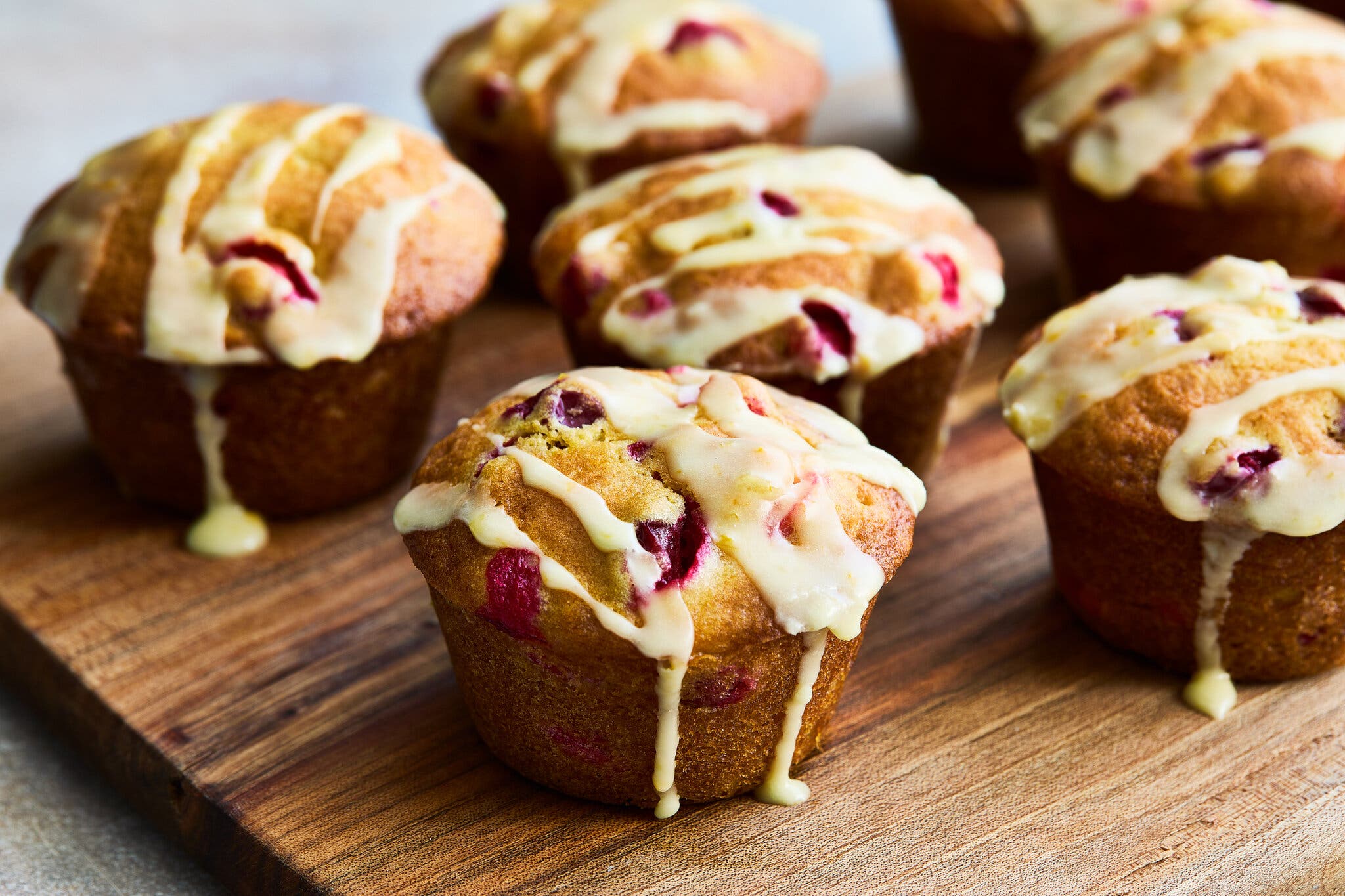 Muffins drizzled with icing sit on a wooden board.