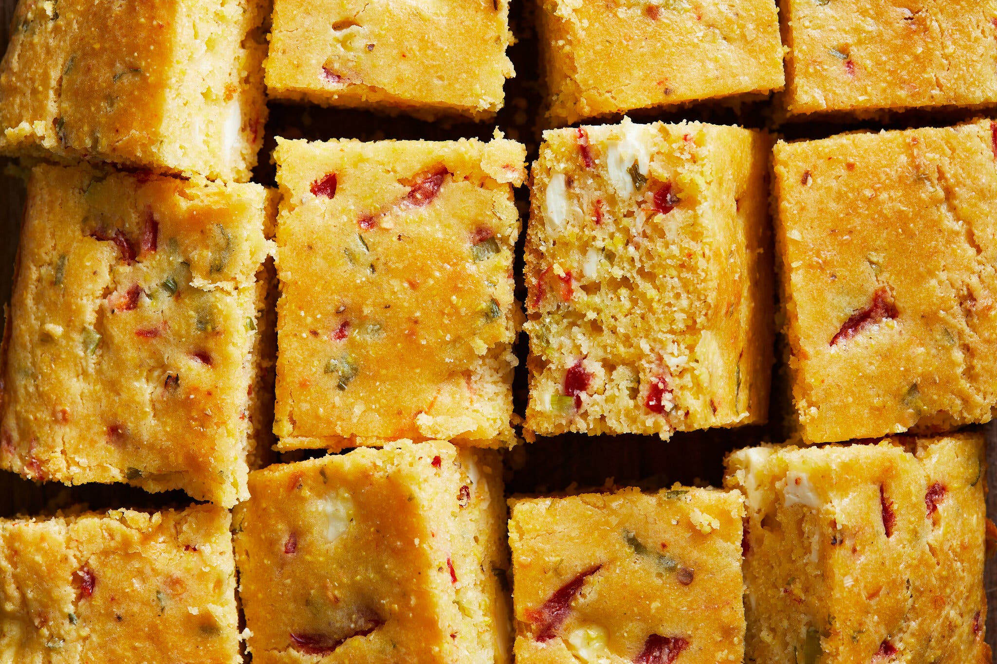 A grid of cornbread squares is studded with roasted red pepper and feta.