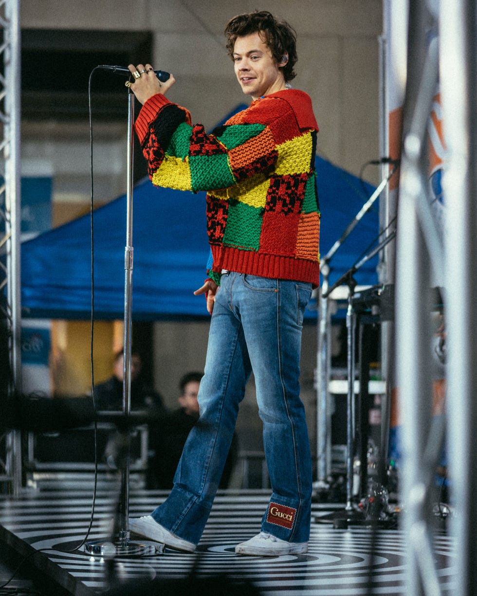 harry styles performing onstage wearing a colorful sweater and jeans