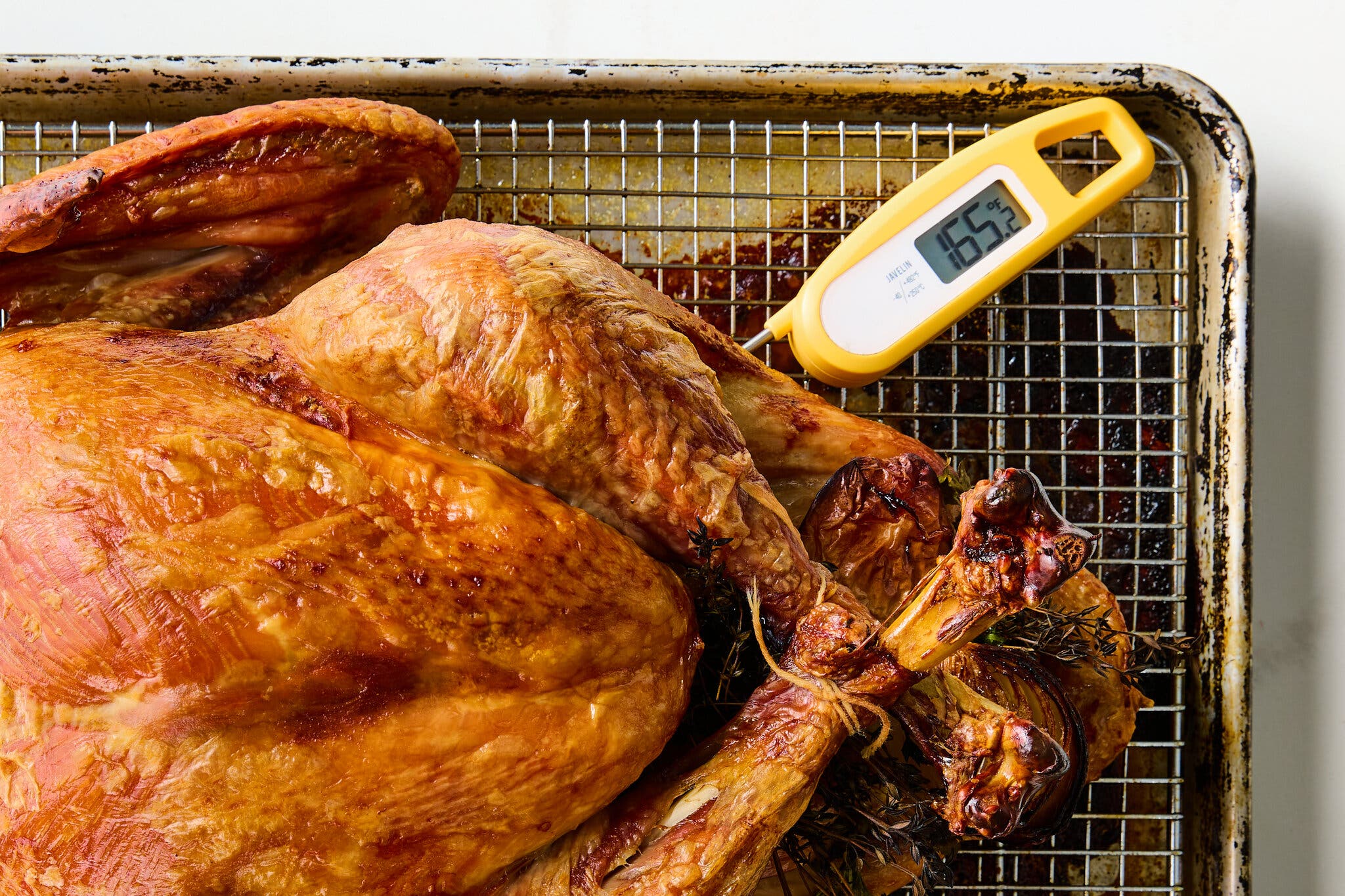 An overhead image of a turkey on a sheet pan. A digital thermometer inserted in its thigh reads 165.2 degrees.