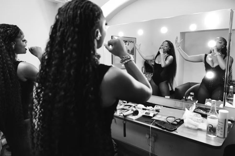 a dressing area with a mirrored table and a person preparing surrounded by makeup items