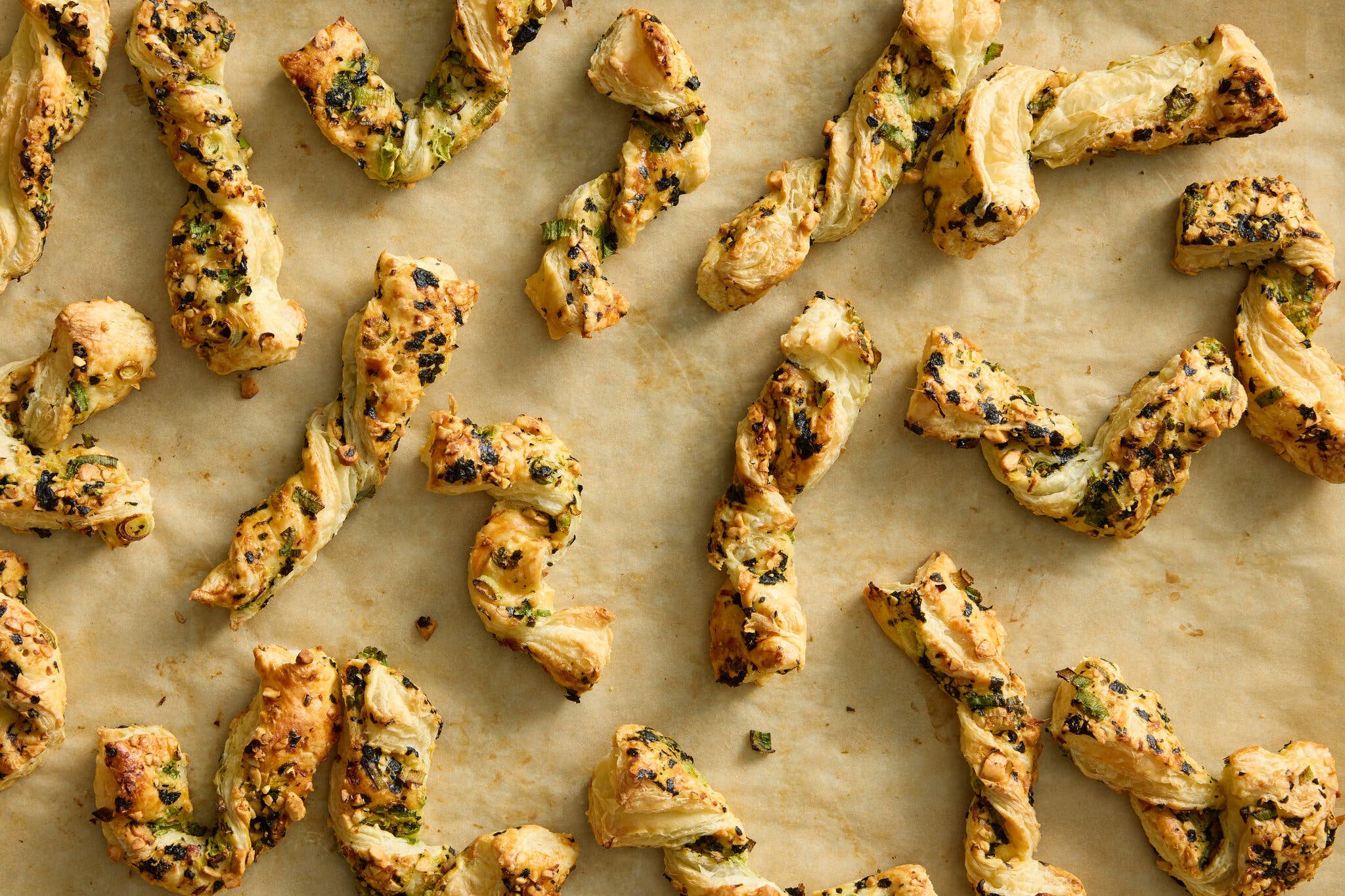 Puff pastry curls finished with sesame and scallion lay on a sheet of parchment paper.