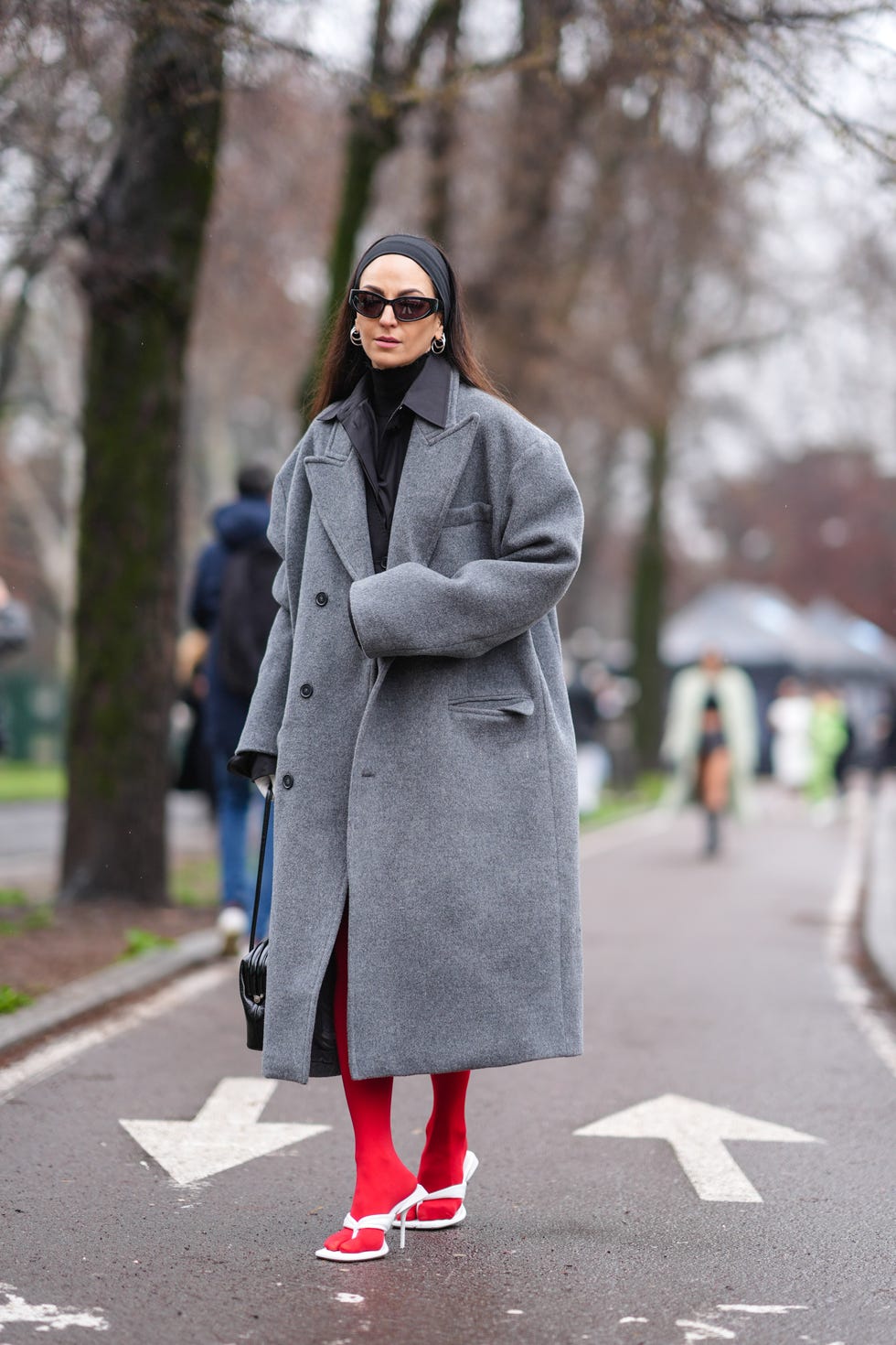 milan, italy february 23 ilenia toma wears a black headband, a black turtleneck, a black shirt, a grey oversized trench coat, red tights, white high heels, a black leather bag, sunglasses, outside tods, during the milan fashion week womenswear fallwinter 2024 2025 on february 23, 2024 in milan, italy photo by edward berthelotgetty images