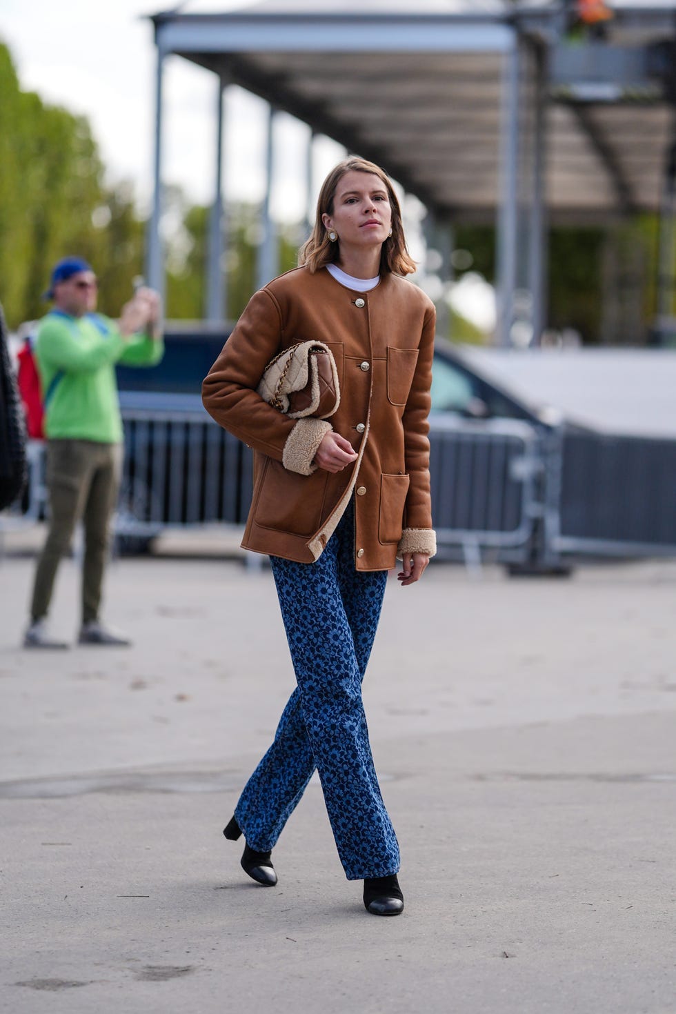 paris, france october 01 monica ainley wears gold earrings, white t shirt, dark brown suede coat with gold buttons, light brown dark brown quilted chanel leather bag, dark blue floral pattern denim jean pants, shiny black heeled leather boots, outside chanel, during the paris fashion week springsummer 2025 on october 1, 2024 in paris, france photo by edward berthelotgetty images