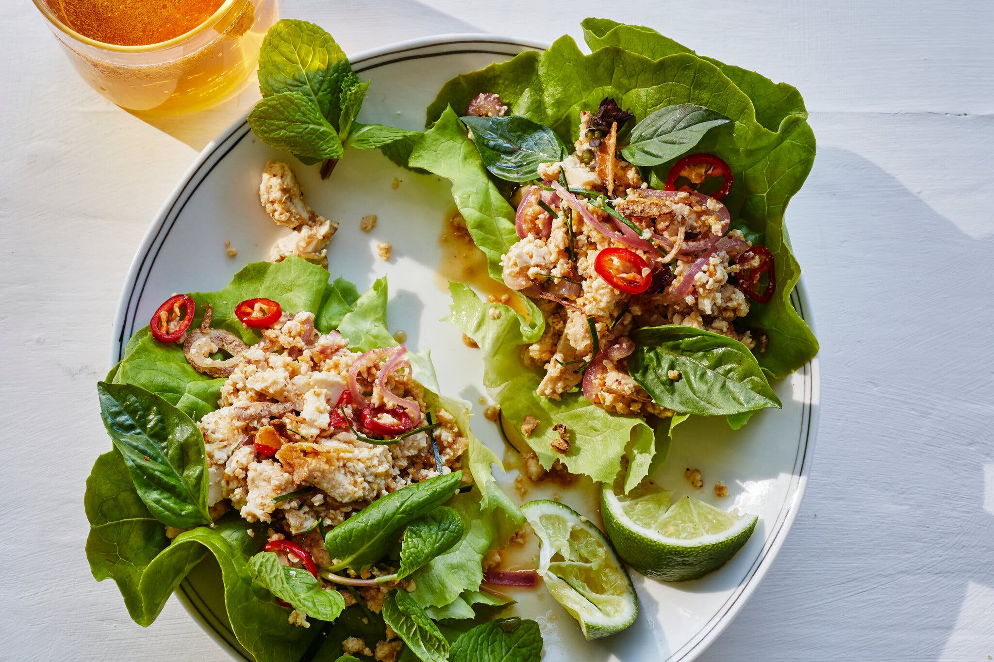 A platter topped with lettuce and ground tofu larb. A couple of lime wedges sit to the side.