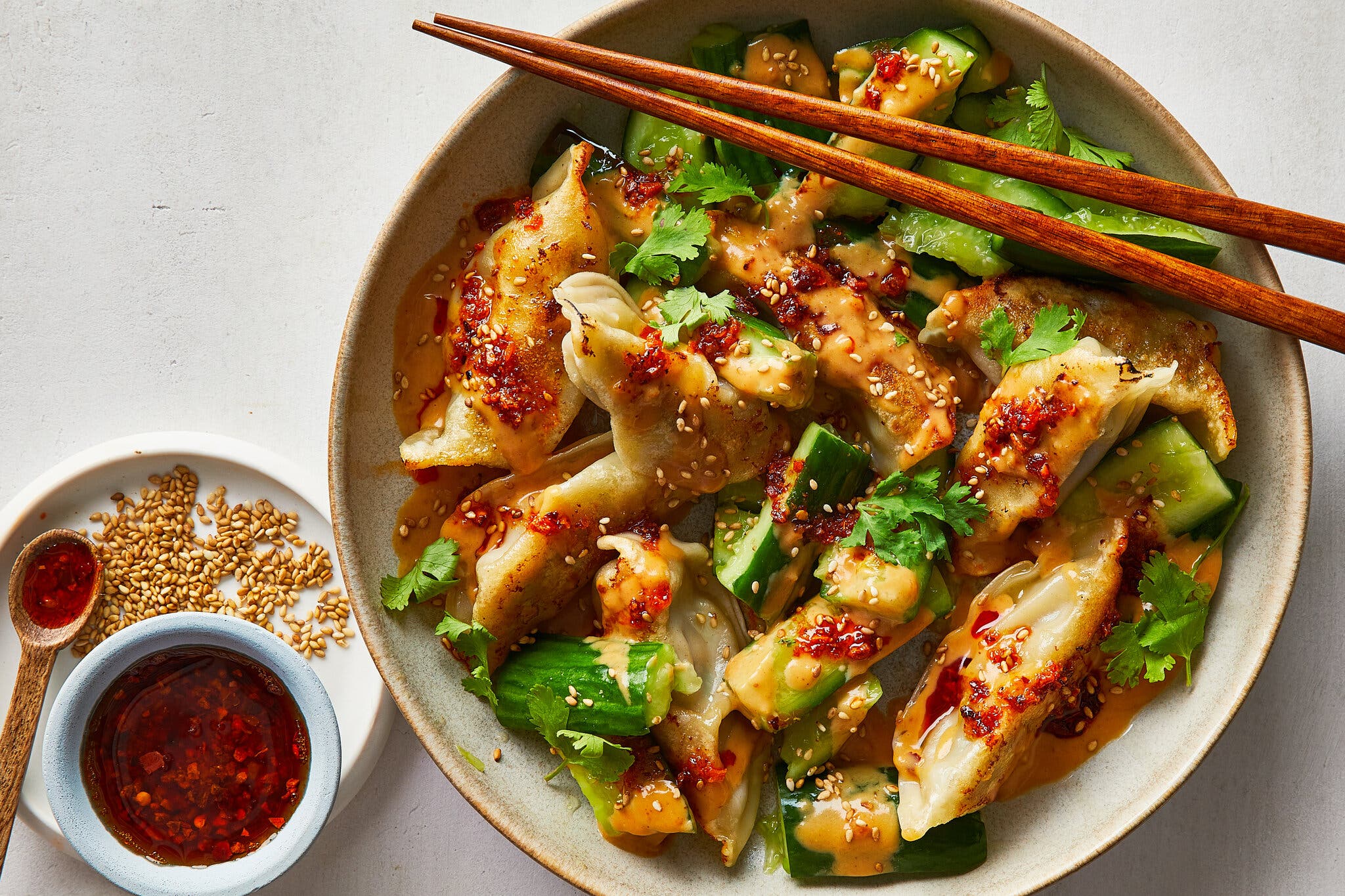 A platter of seared dumplings and crushed cucumbers. A small bowl filled with chili crisp sits nearby.