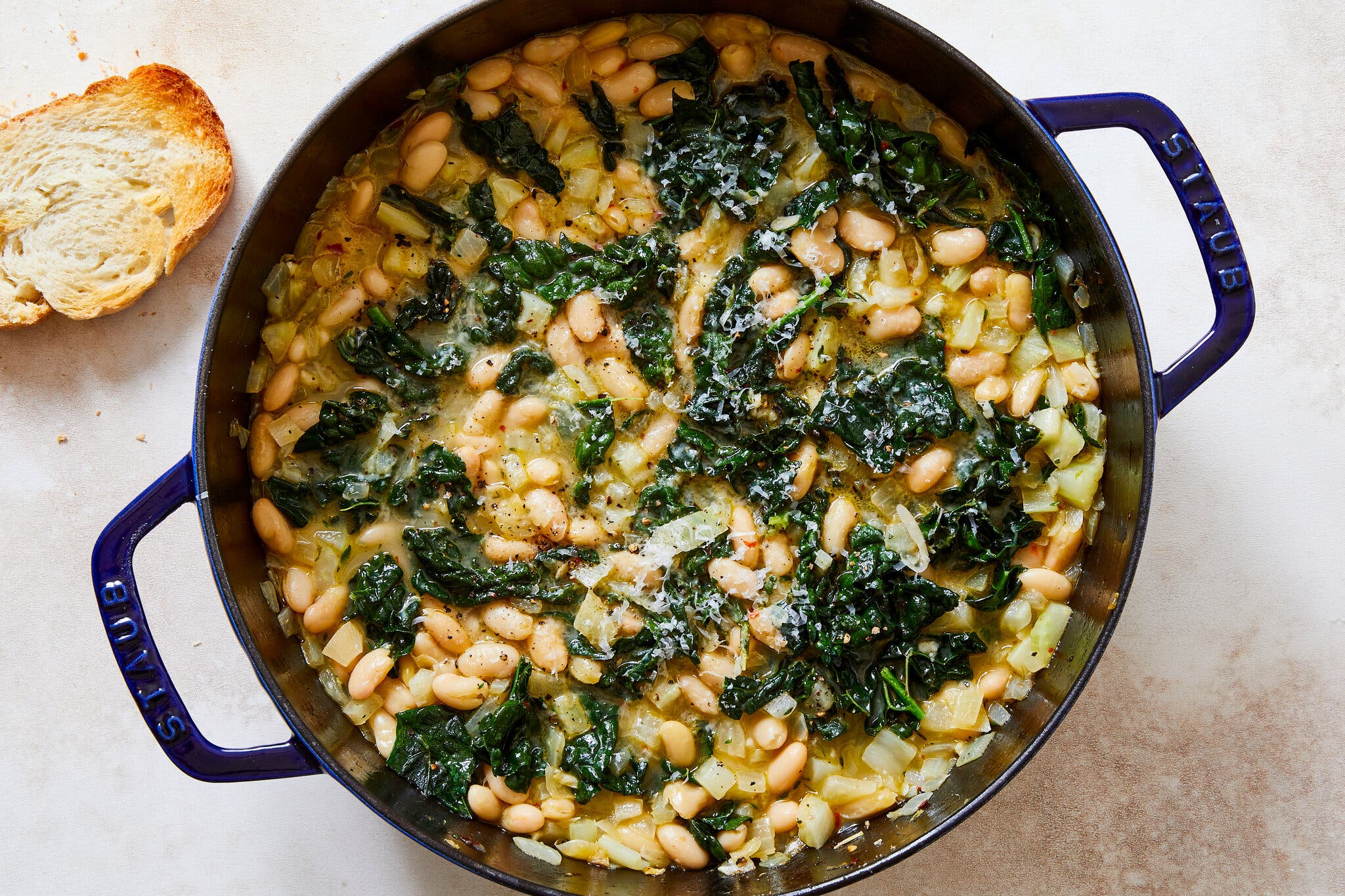 A large Dutch oven full of beans and greens sits against an off-white surface.